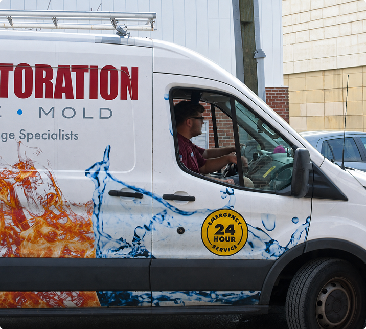 Restoration service van with driver, featuring emergency 24-hour badge and contact numbers on the side