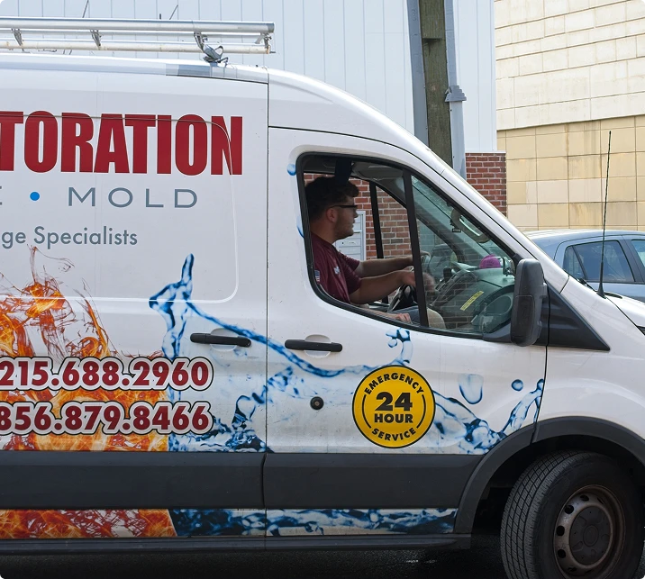 Restoration service van with driver, featuring emergency 24-hour badge and contact numbers on the side